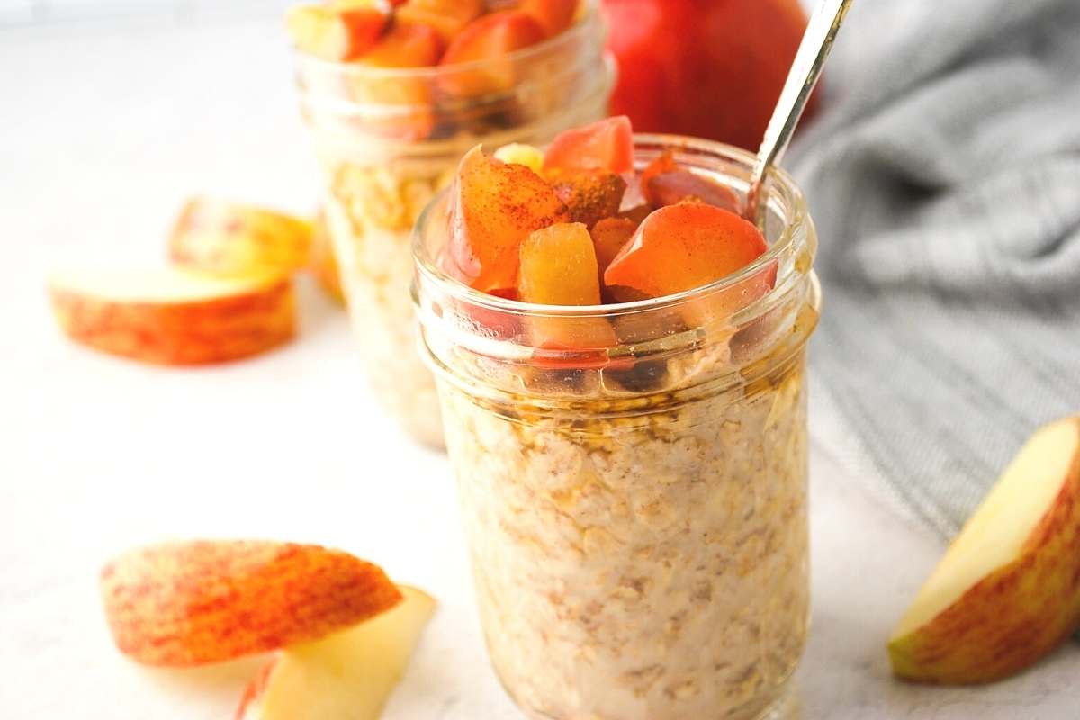 apple pie overnight oats in a jar with a spoon with sliced apples around it