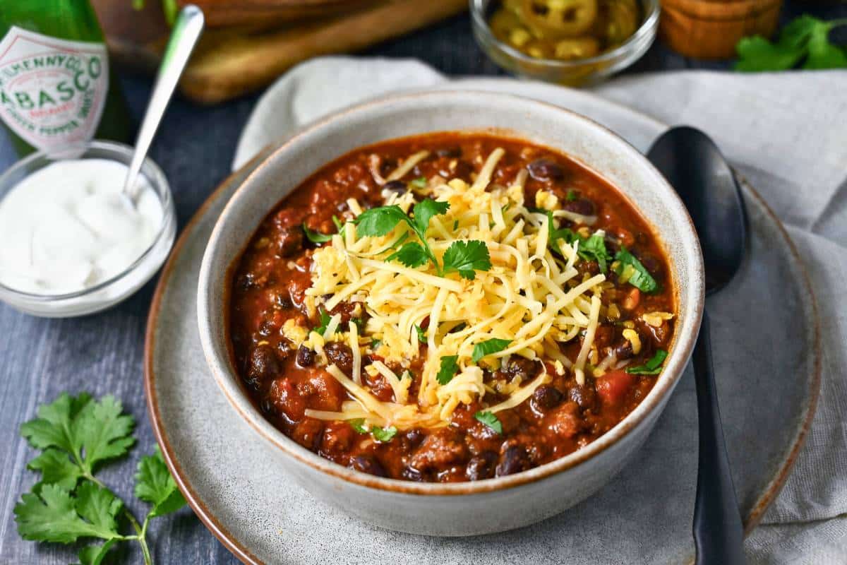 side view of a bowl of chili and a side of sour cream with fresh cilantro