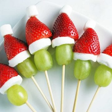 green grapes, marshmallows, and strawberries on skewers to look like a Grinch face with a Santa hat