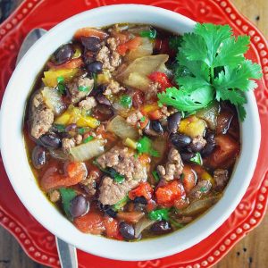 bowl of chili on a red plate with a sprig of fresh herbs