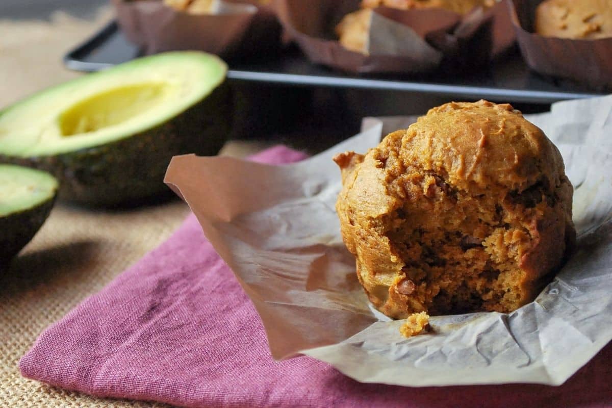 close up of an avocado muffin with a bite taken out of it with a sliced avocado