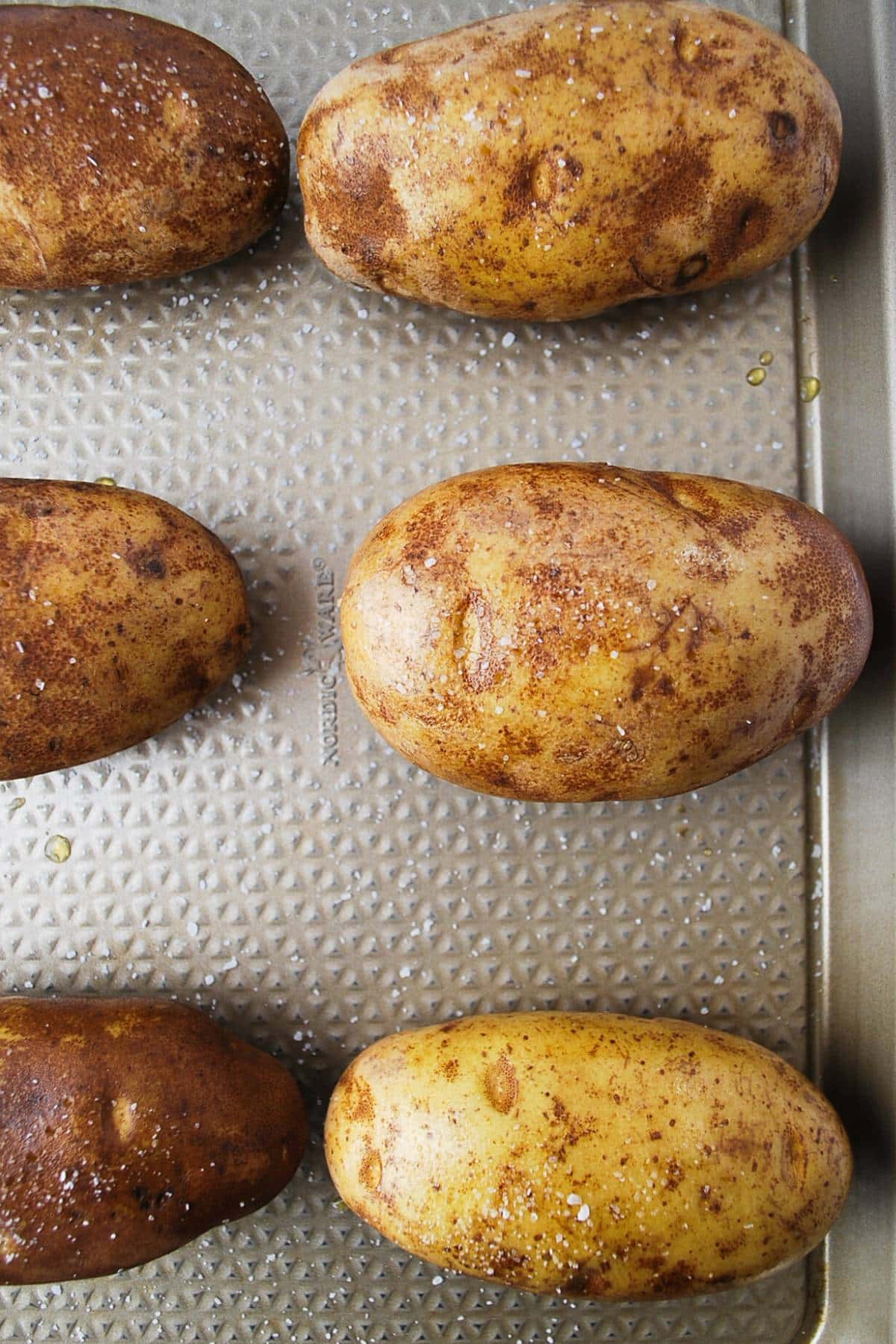 baked potatoes sprinkled with coarse salt on a baking sheet