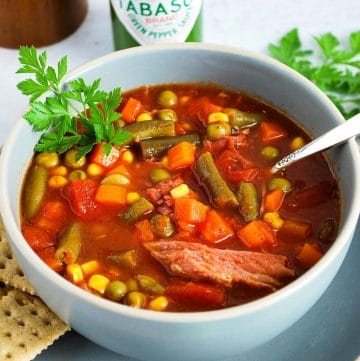 a bowl of ham vegetable soup with parsley and crackers