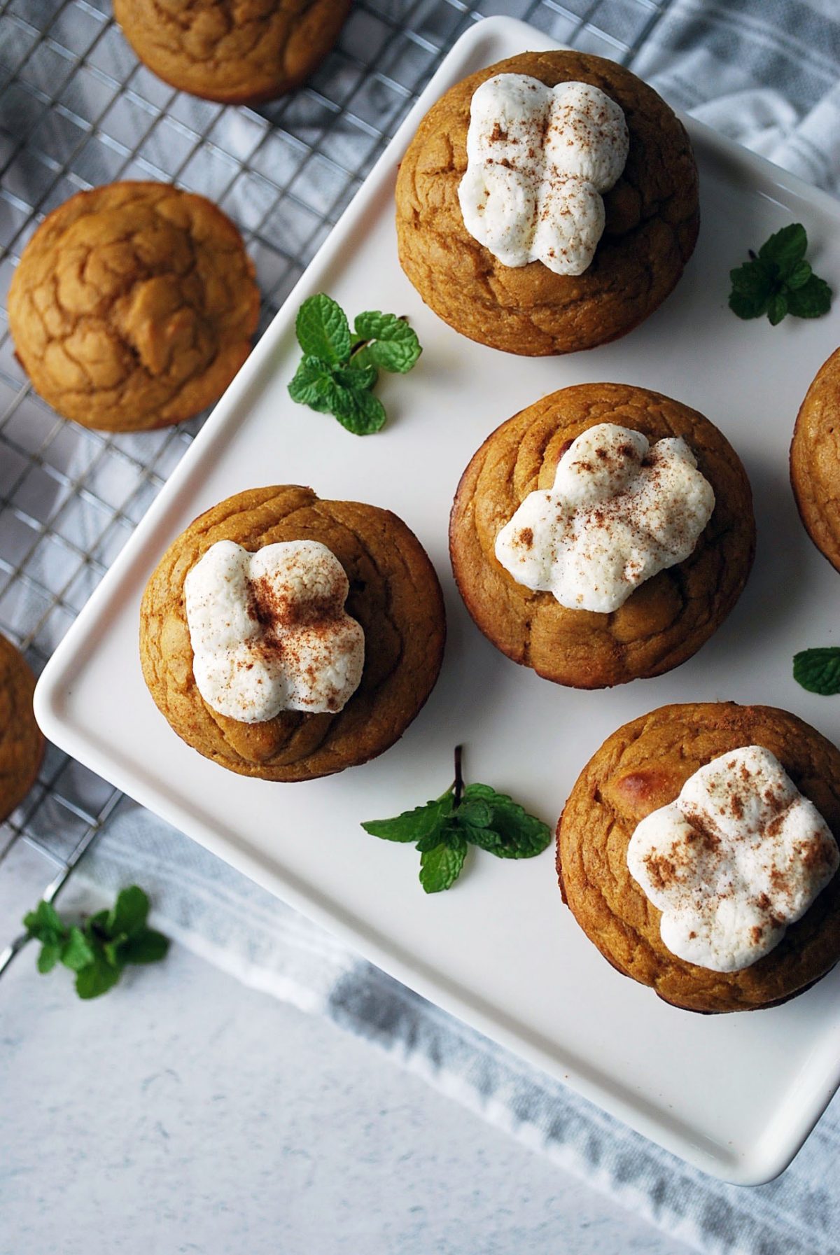 overhead photo of sweet potato muffins on a white platter topped with marshmallows with muffins on a cooling rack in the background
