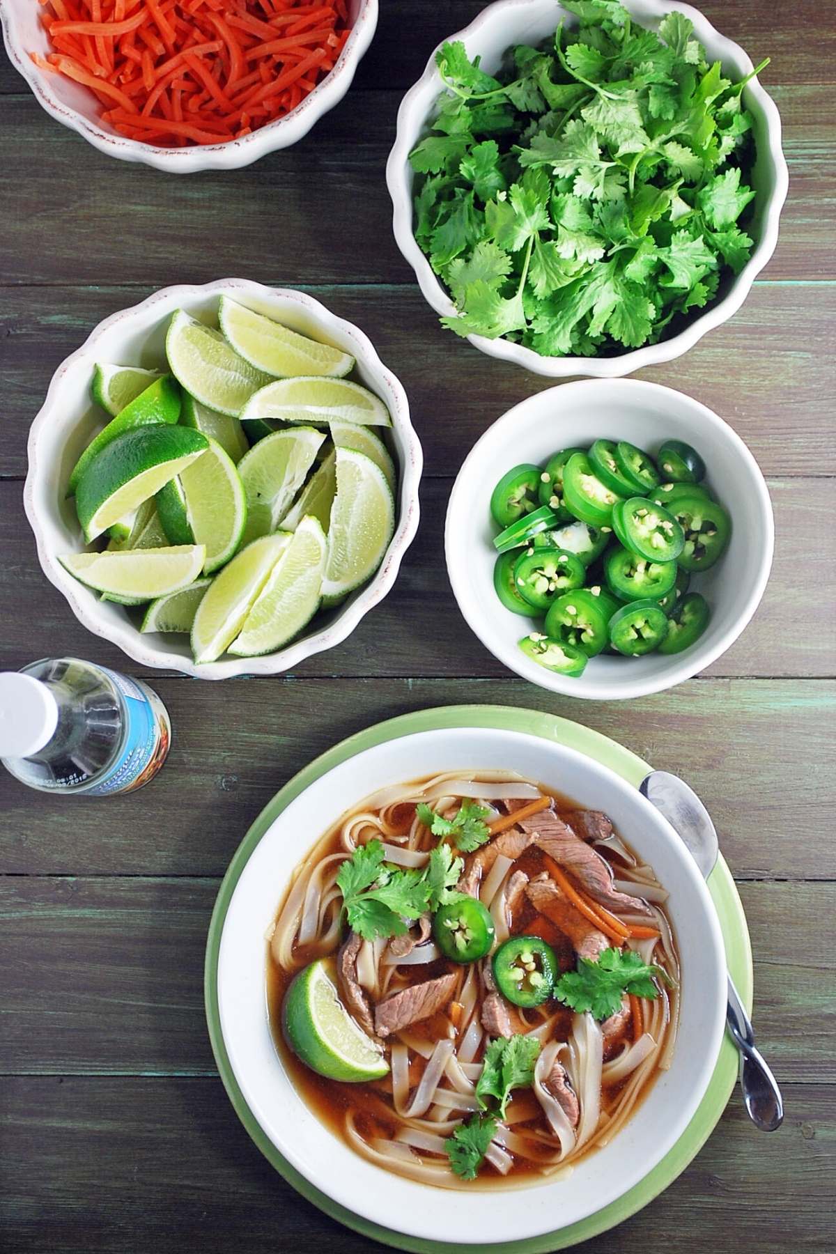 a bowl of flank steak pho with bowls of toppings to choose from