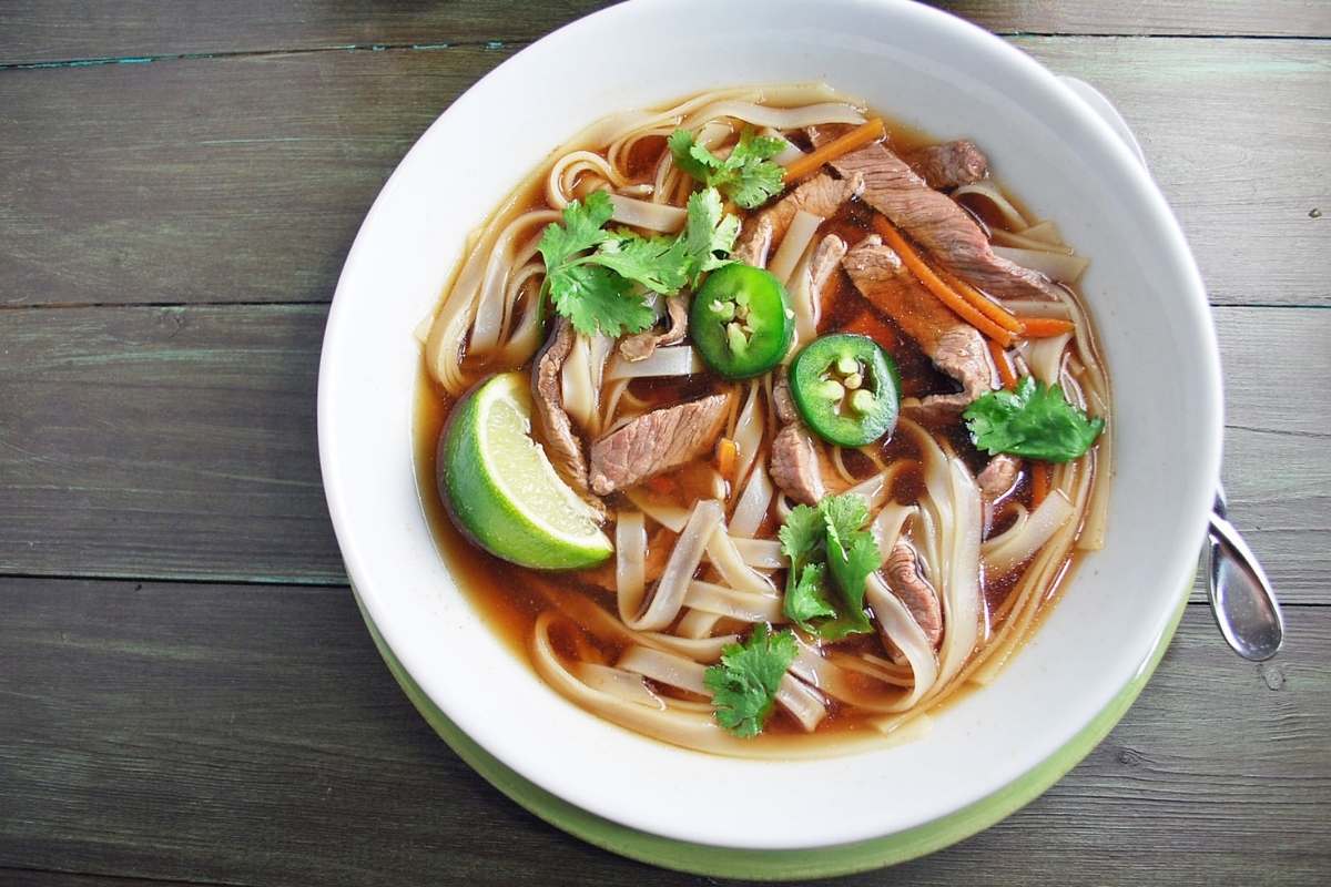 a bowl of flanks steak pho with a slice of lime