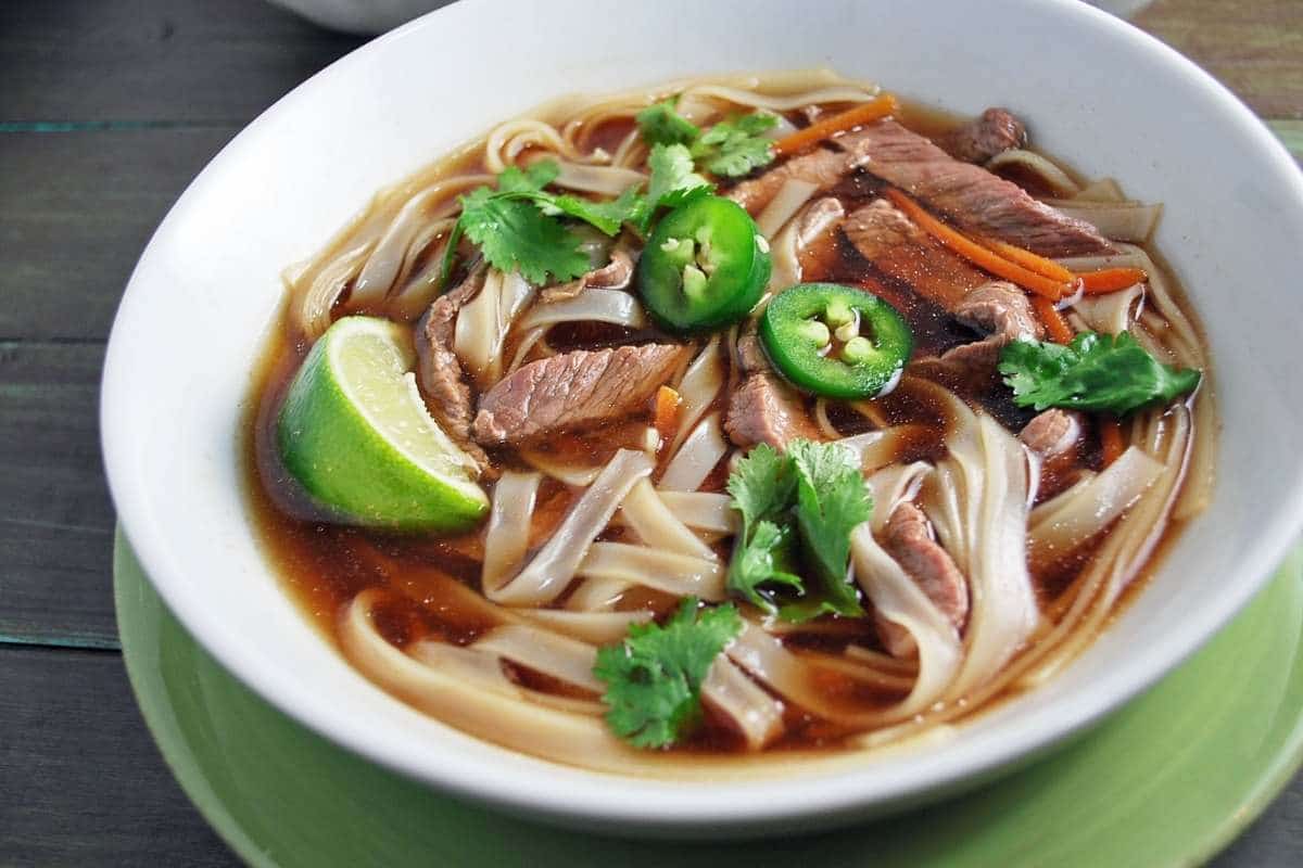 close up of a bowl of flank steak pho with fresh jalapenos and lime