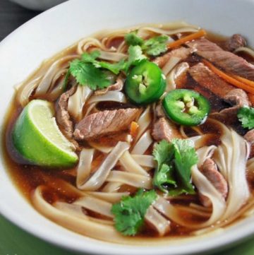 bowl of beef pho made with broth, noodles, steak, fresh cilantro, carrots, jalapenos, and lime