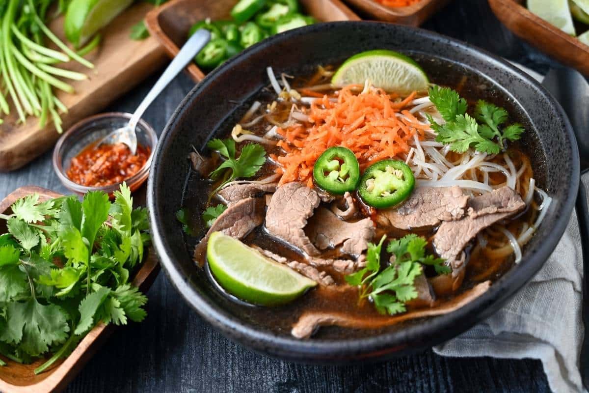 a bowl of loaded flank pho with all the toppings around it