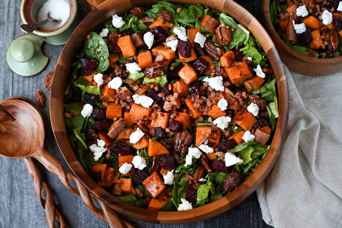 a bowl of beet sweet potato salad with goat cheese, pecans, and pancetta with salad tongs and a jar of salt