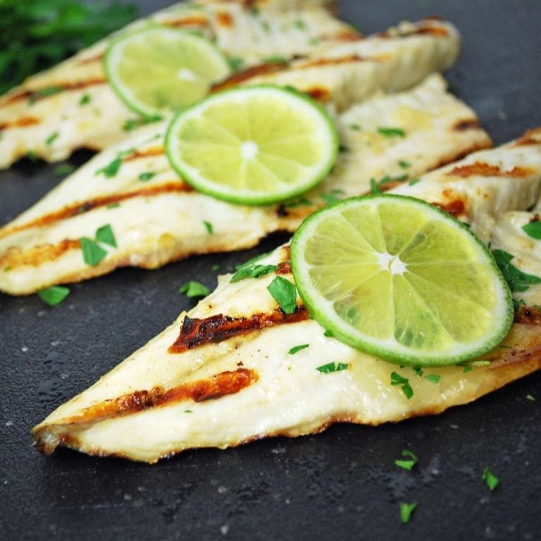 three grilled fish filets on a black cutting board topped with a slice of lime