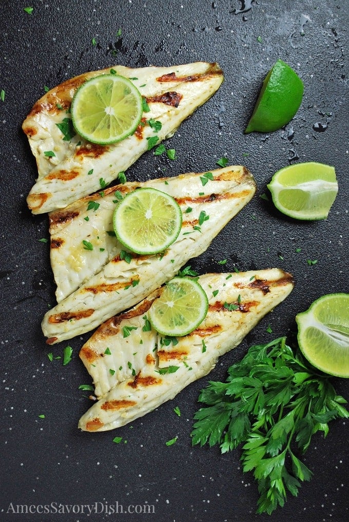 Overhead photo of sea bass on a cutting board with fresh herbs and limes