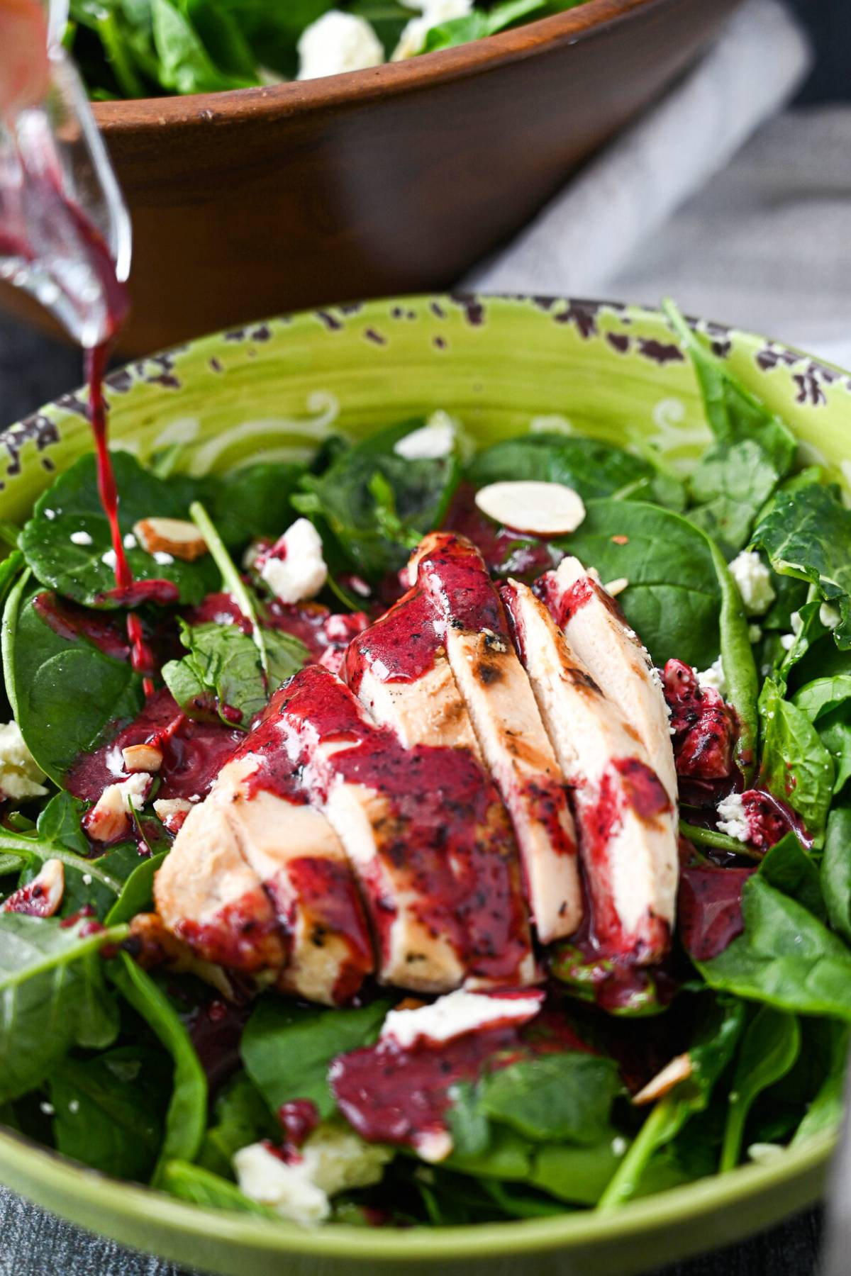 kale and spinach salad with a chicken breast with blueberry vinaigrette dressing being poured on top