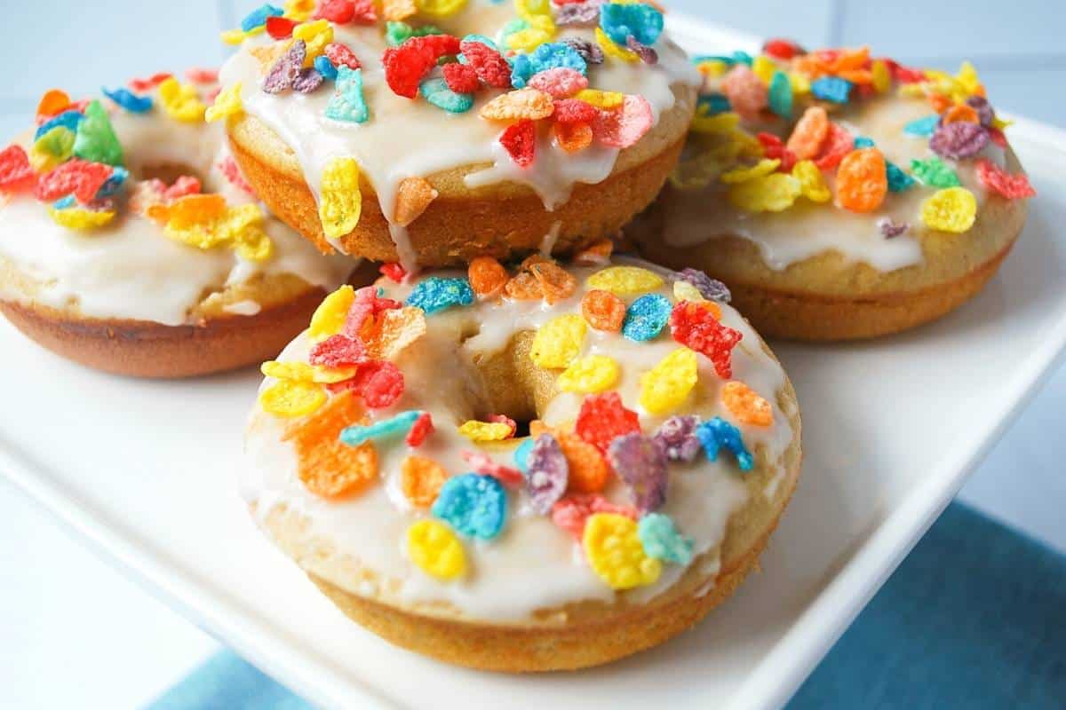 vanilla protein donuts on a white platter topped with glaze and Fruity Pebble cereal
