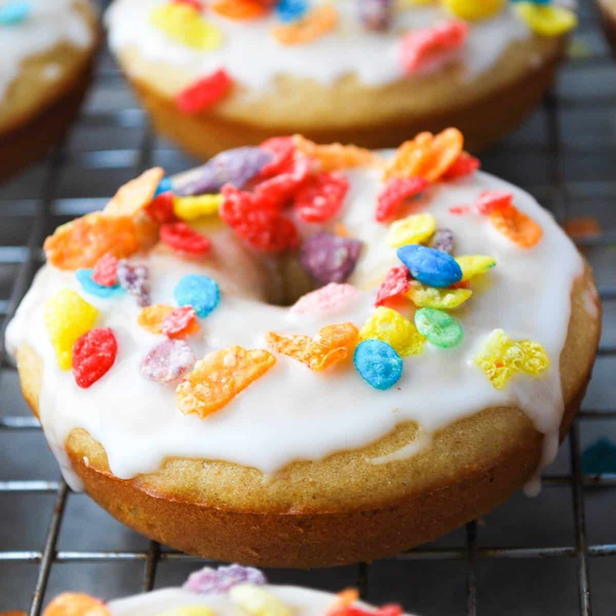 a vanilla protein donut with glaze and fruity cereal on a cooling rack
