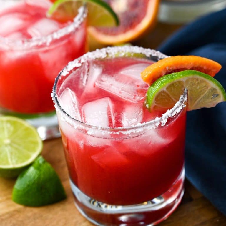 close up of a blood orange vodka cocktail with ice and a blood orange and lime slice on a salted rim