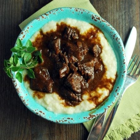 Bowl of Mediterranean beef over cauliflower mashed potatoes in a bowl with silverware and green napkin