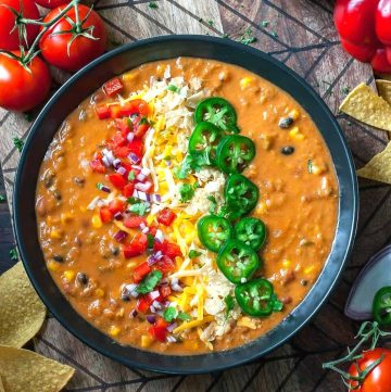 A bowl of lentil soup topped with cheese, fresh jalapenos, and tomatoes