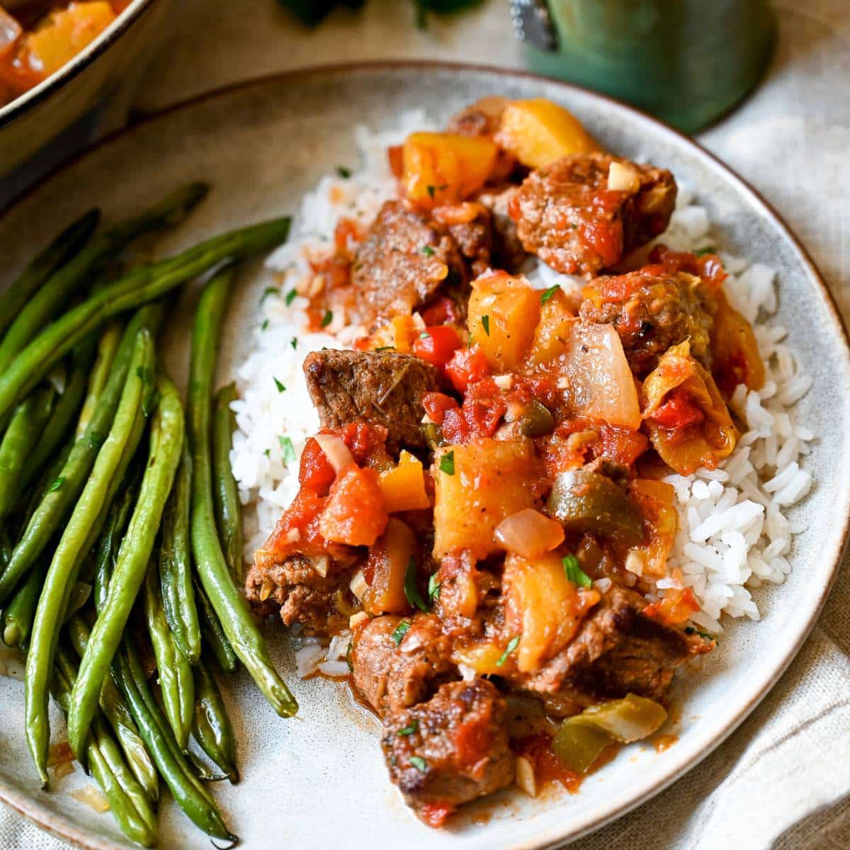 a heaping serving of mango beef over rice with green beans on a plate