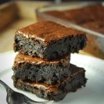 chocolate browines stacked on a white plate with pan of brownies in the background