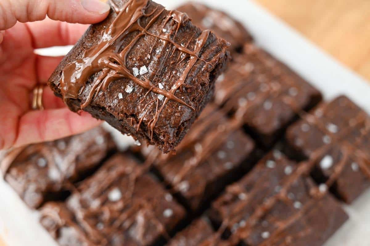 holding up a sliced brownie with sliced brownies in the background