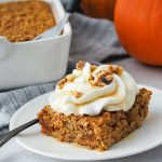 a square slice of pumpkin baked oats with whipped cream and nuts with a pumpkin in the background