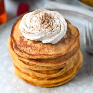 a stack of sweet potato pancakes with whipped cream and cinnamon on top