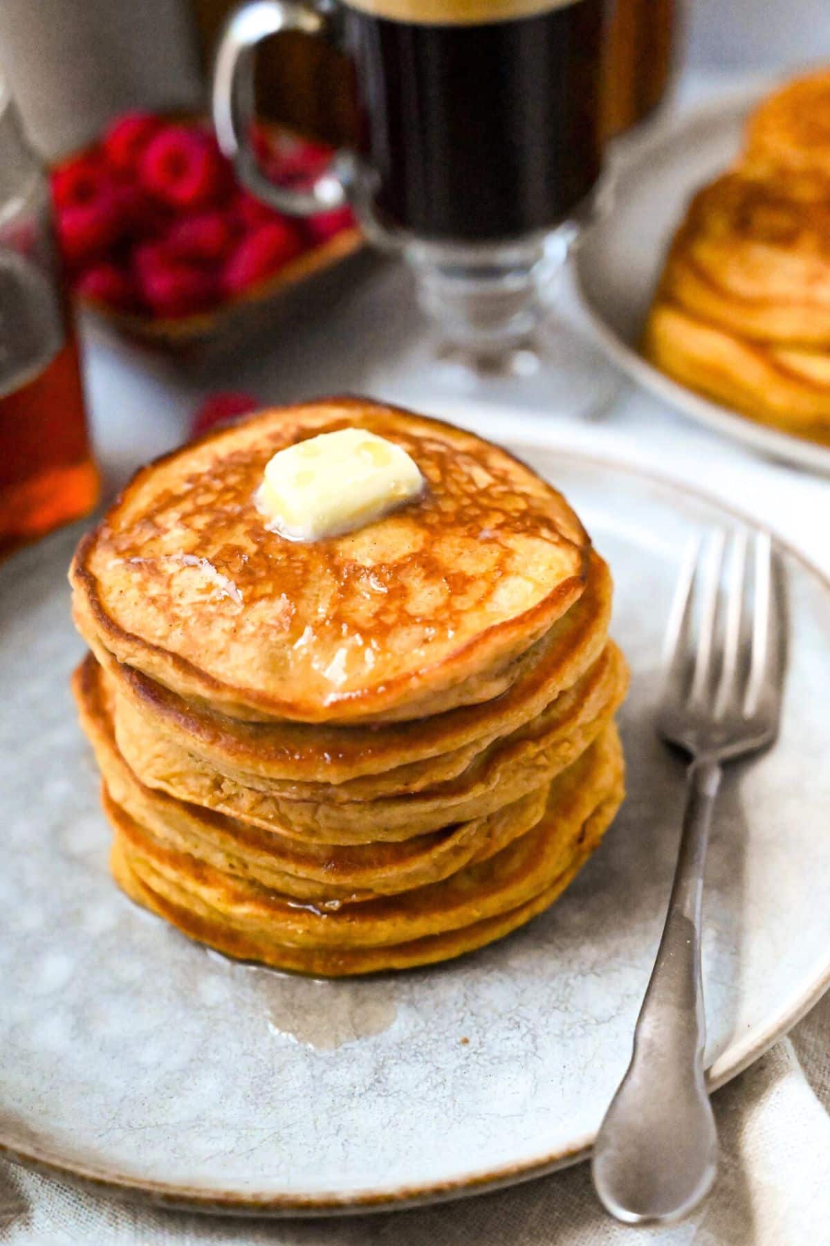 a tall stack of pancakes with butter and syrup with a fork on a plate