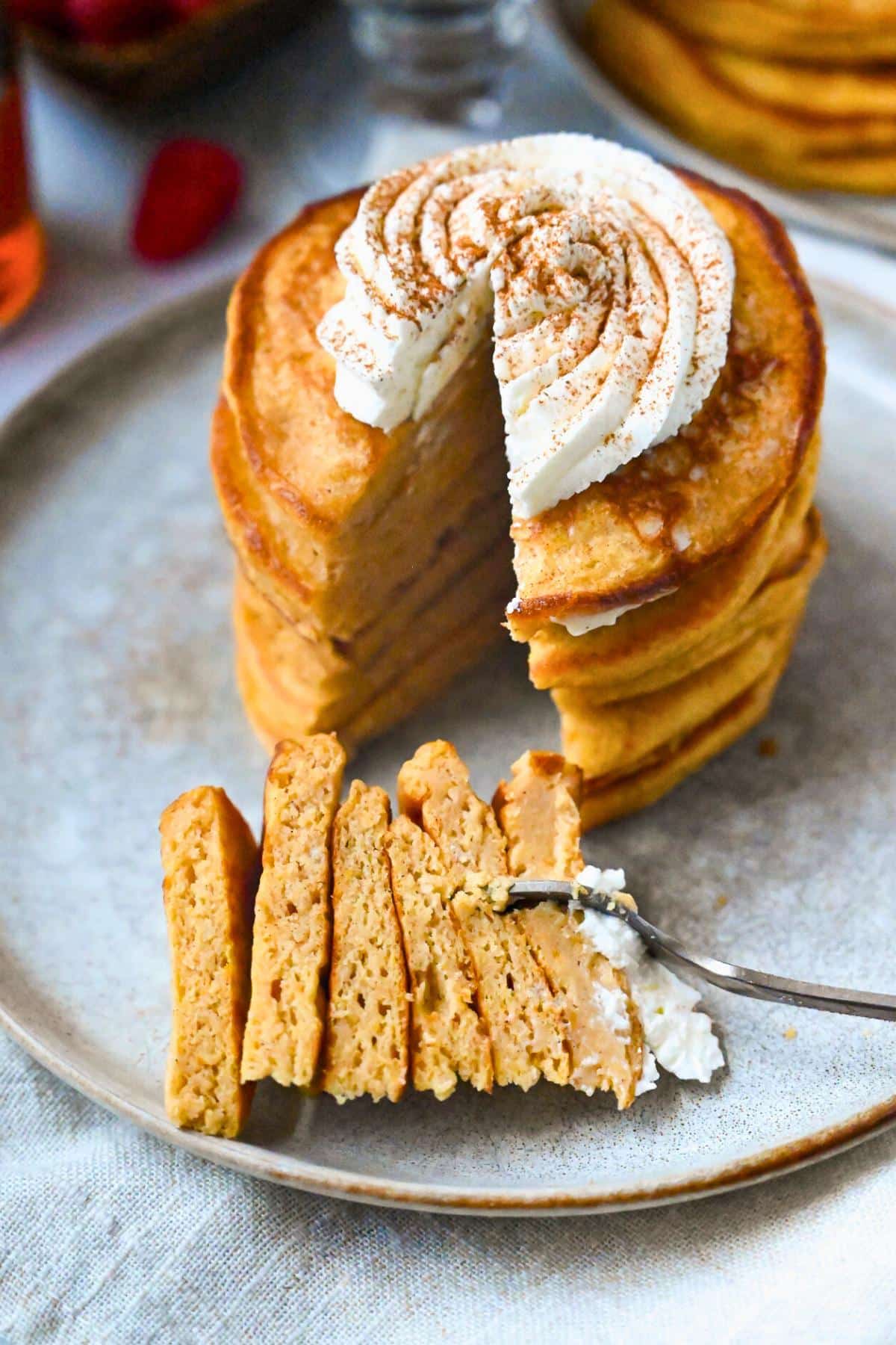 a stack of pancakes with whipped cream with a wedge cut out with a fork