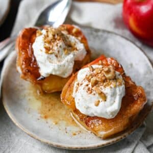 two apple halves that have been air fried and topped with yogurt and nuts with an apple in the background