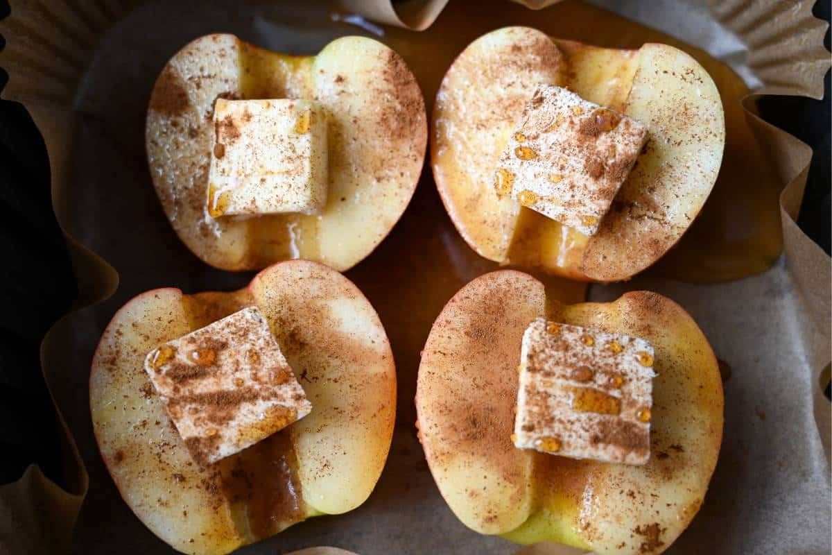 apple halves topped with a pat of butter, cinnamon and maple syrup in an air fryer basket