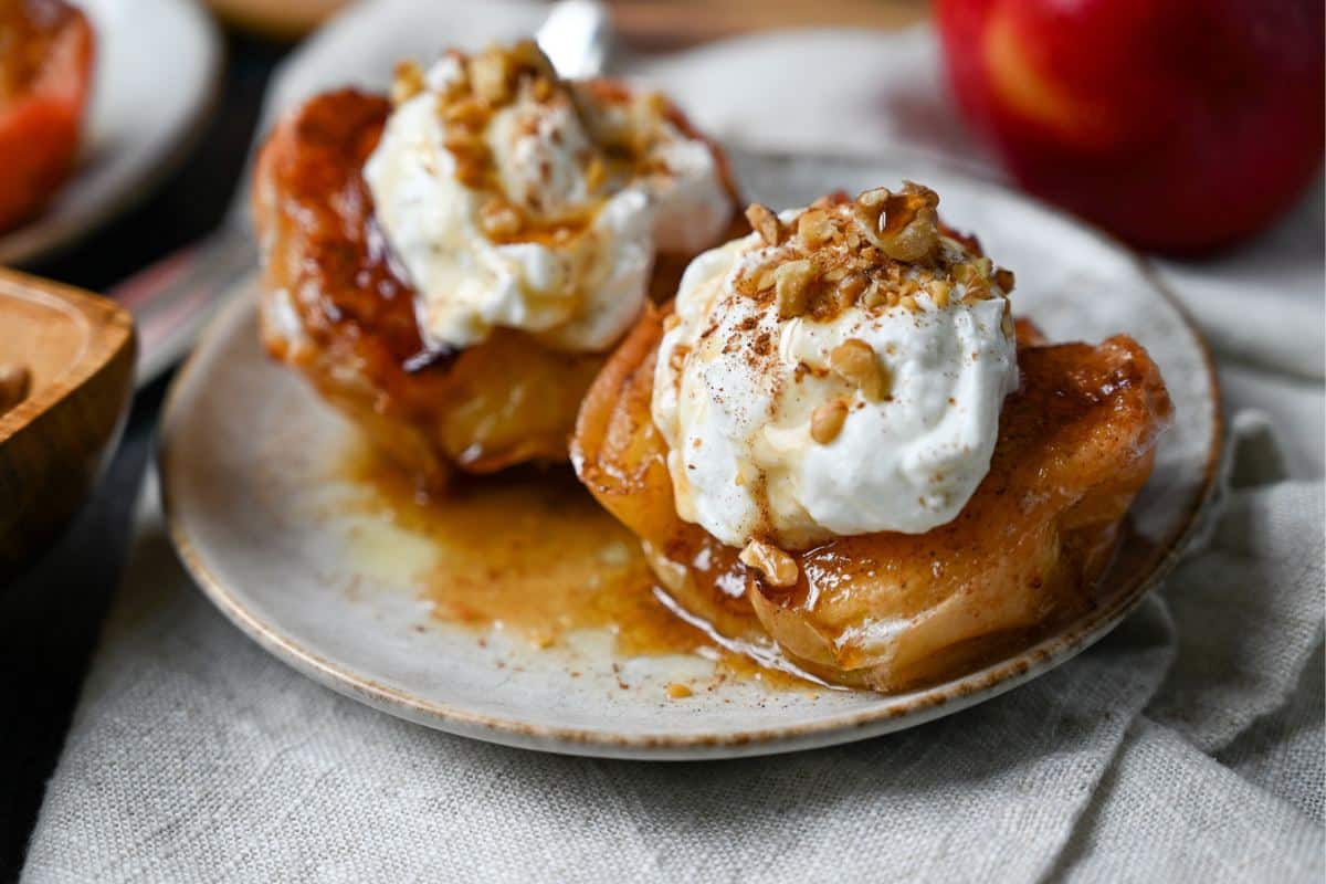 apple halves drizzled with a butter maple topping with yogurt and nuts on a plate