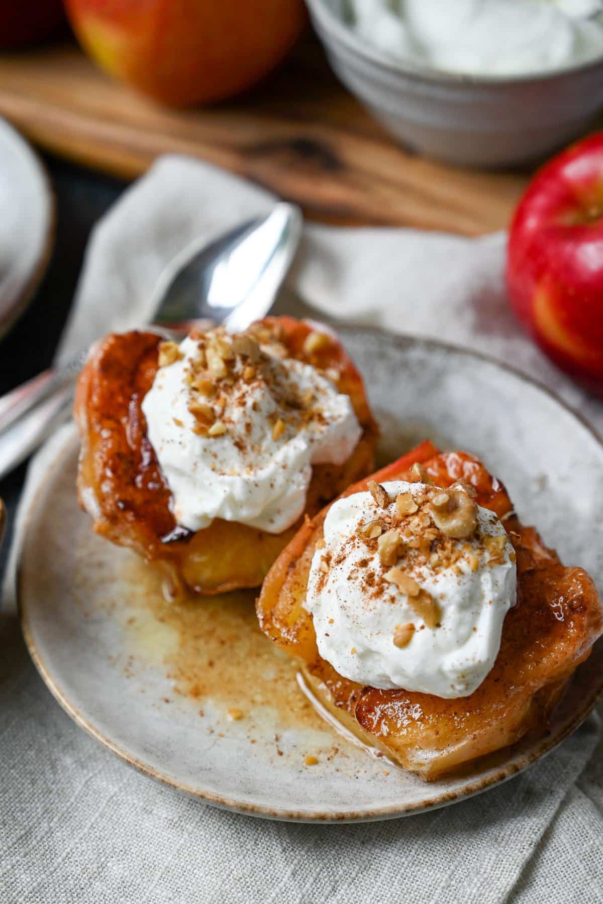 looking down at a plate of air fried apples with yogurt and nut topping with apples and a bowl of yogurt behind it