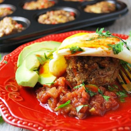Southwest Beef Breakfast Muffin on a plate topped with a fried egg and served with slice avocado on a red plate