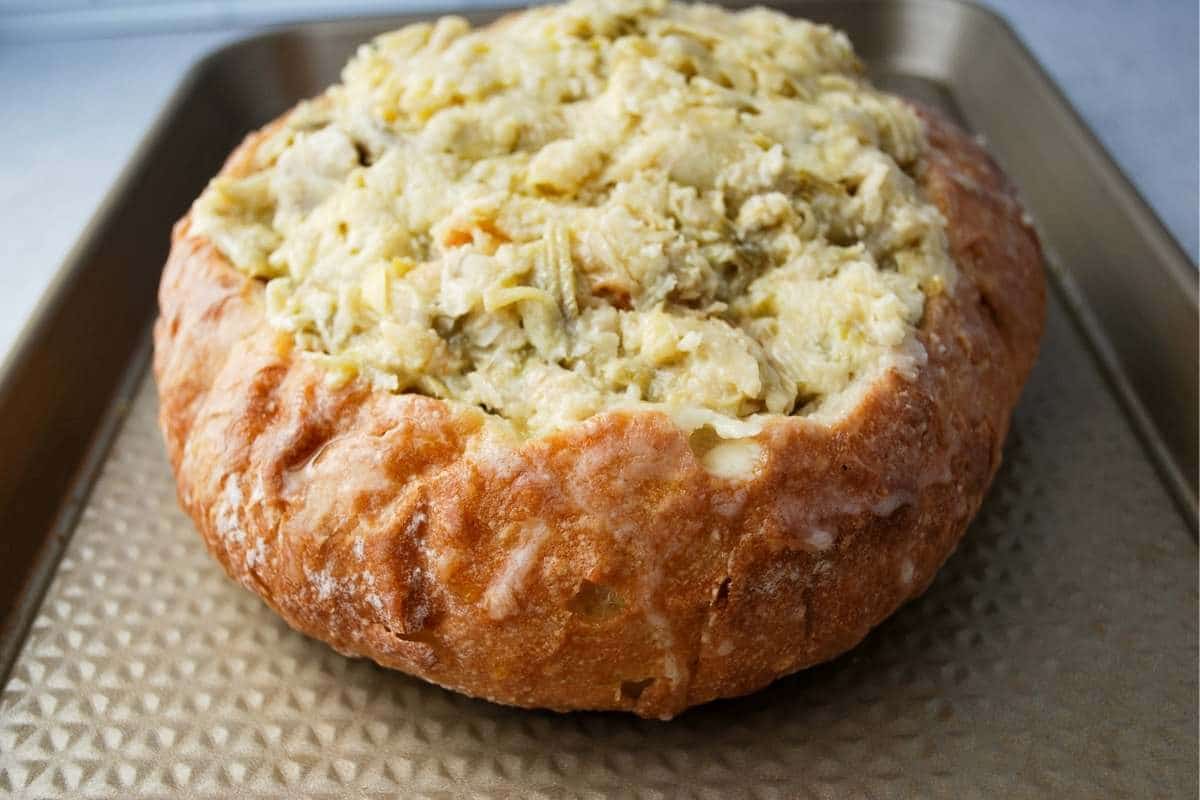 artichoke dip in a bread bowl on a baking sheet