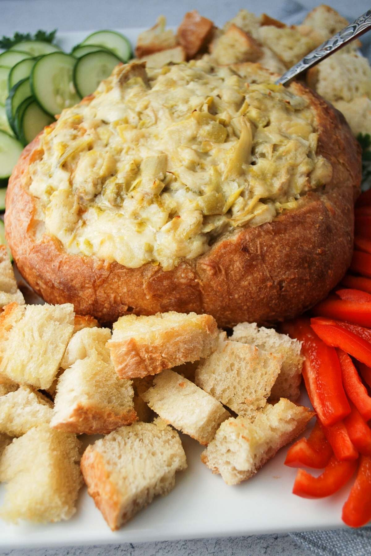artichoke dip baked in a bread bowl with bread cubes and veggies