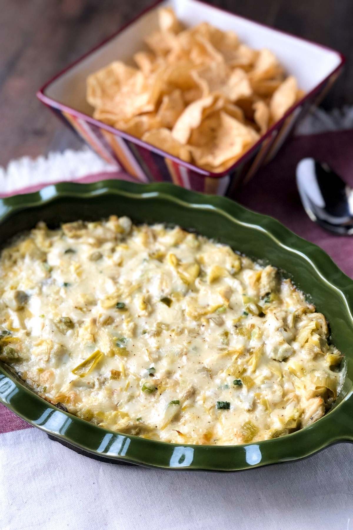 artichoke dip baked in a casserole dip with a bowl of tortilla chips