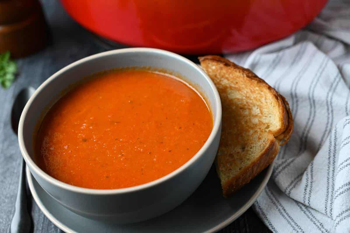 close up of a bowl of tomato bisque made without cream with a grilled cheese and spoon