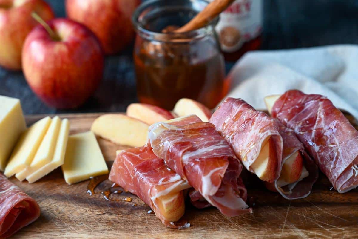 side view of prosciutto-wrapped cheese and apples with sliced cheese and apples next to them
