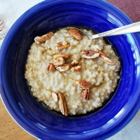 cooked oats topped with syrup and pecans in a blue bowl with a spoon