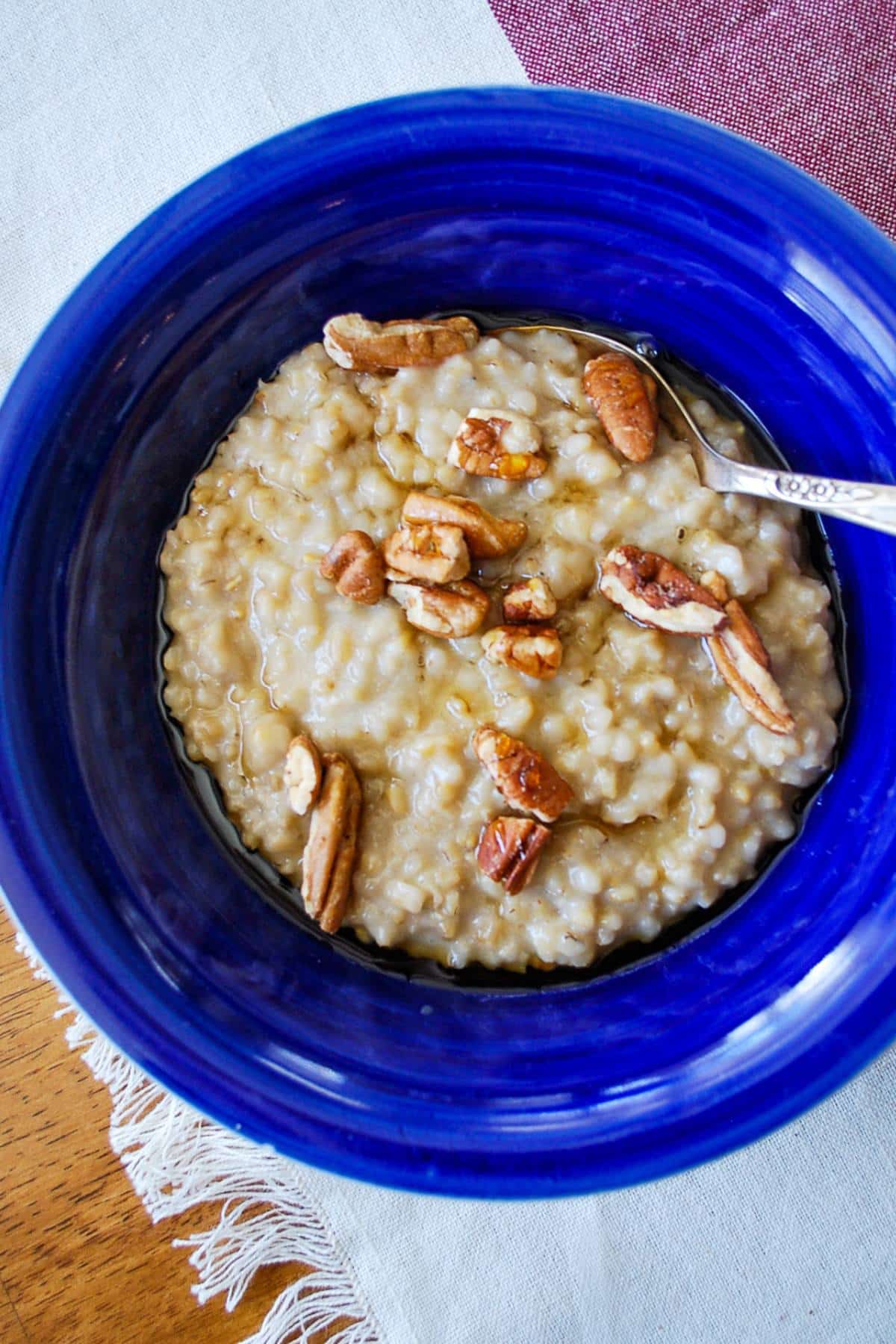 overhead photo of steel cut oats in a blue bowl with pecans, maple syrup and a spoon 
