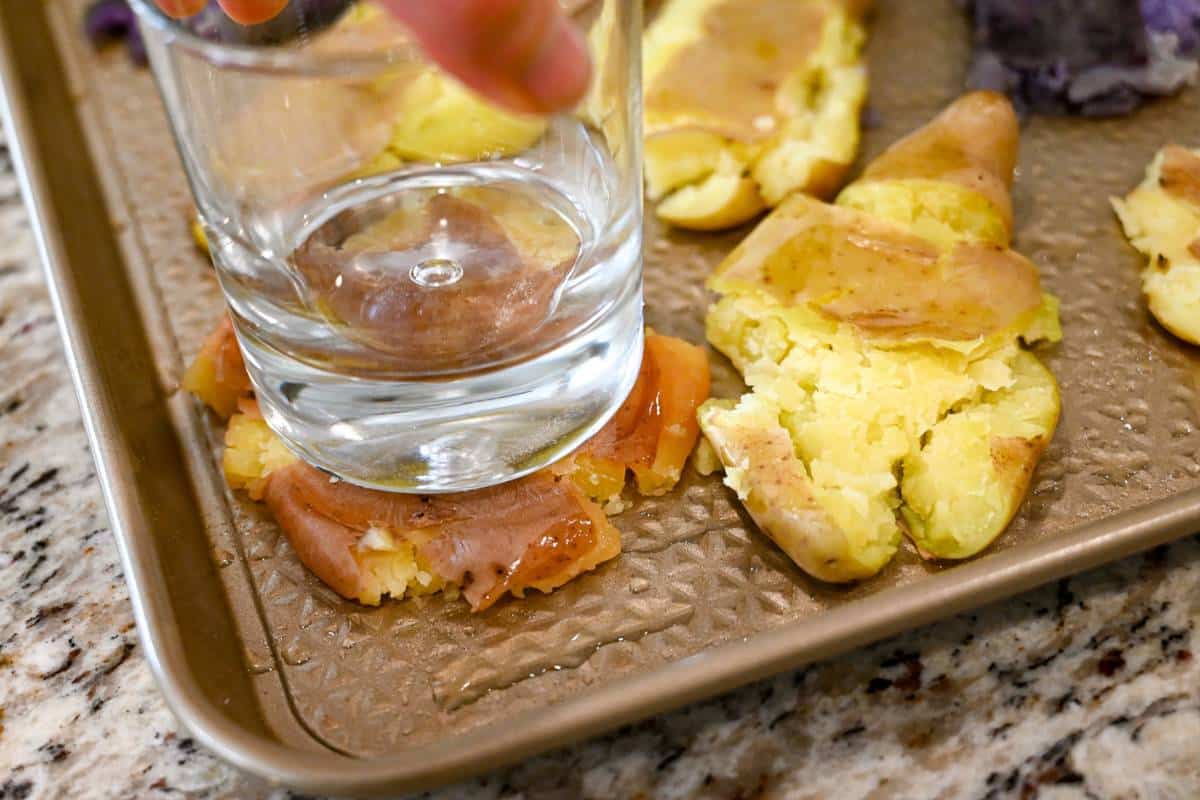 smashing a fingerling potato on a baking sheet with the bottom of a glass