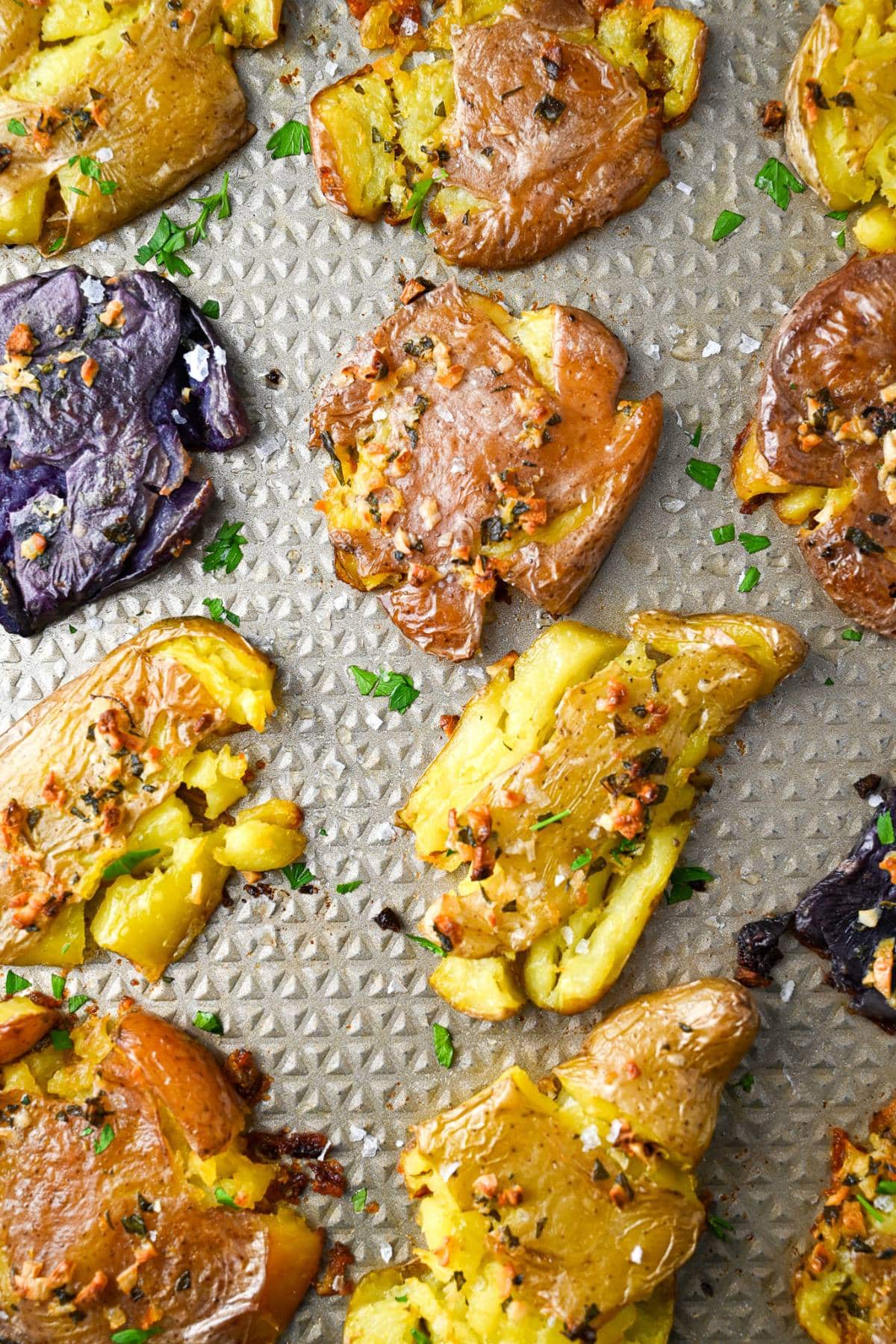 Sheet pan with colorful smashed fingerling potatoes oven-roasted in a Greek herb and olive oil butter mixture.