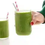 holding up a green smoothie with two straws