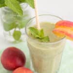 a green smoothie in a glass with a peach slice and mint