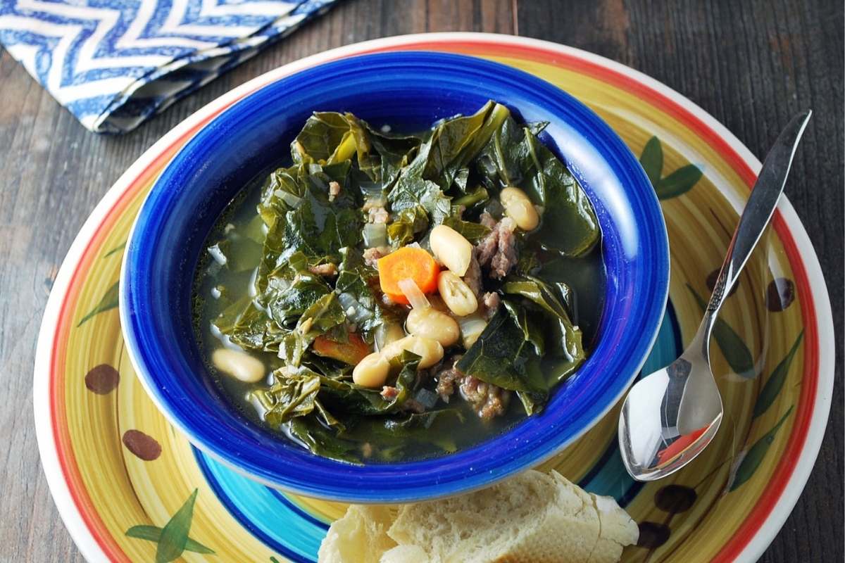 bowl of sausage bean soup with collards with a slice of baguette