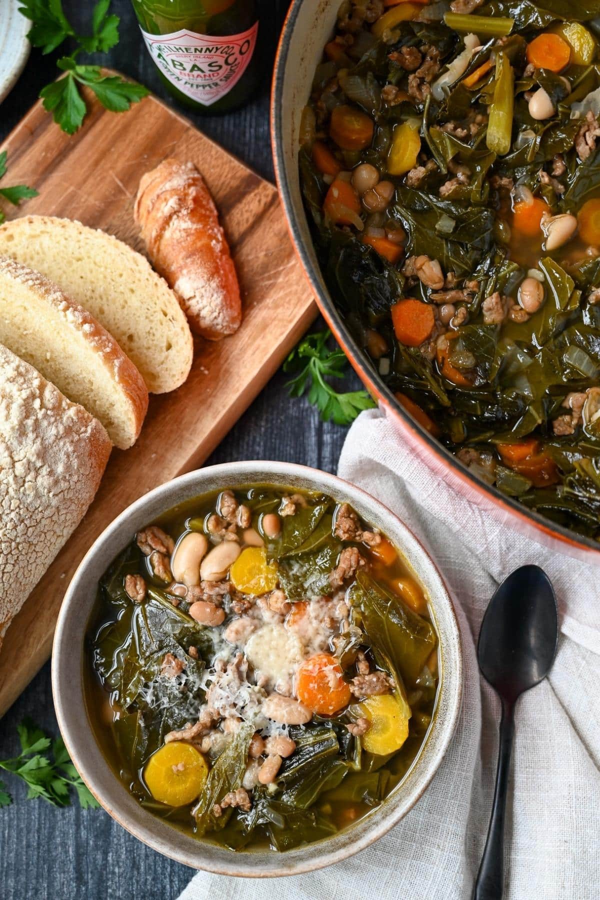 bowl of collard soup with a sliced loaf of homemade bread and a pot of soup next to it