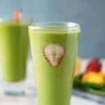 a green smoothie with a sliced strawberry in it