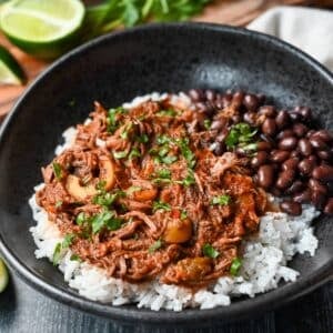 close up of a bowl of shredded cuban beef with black beans and rice