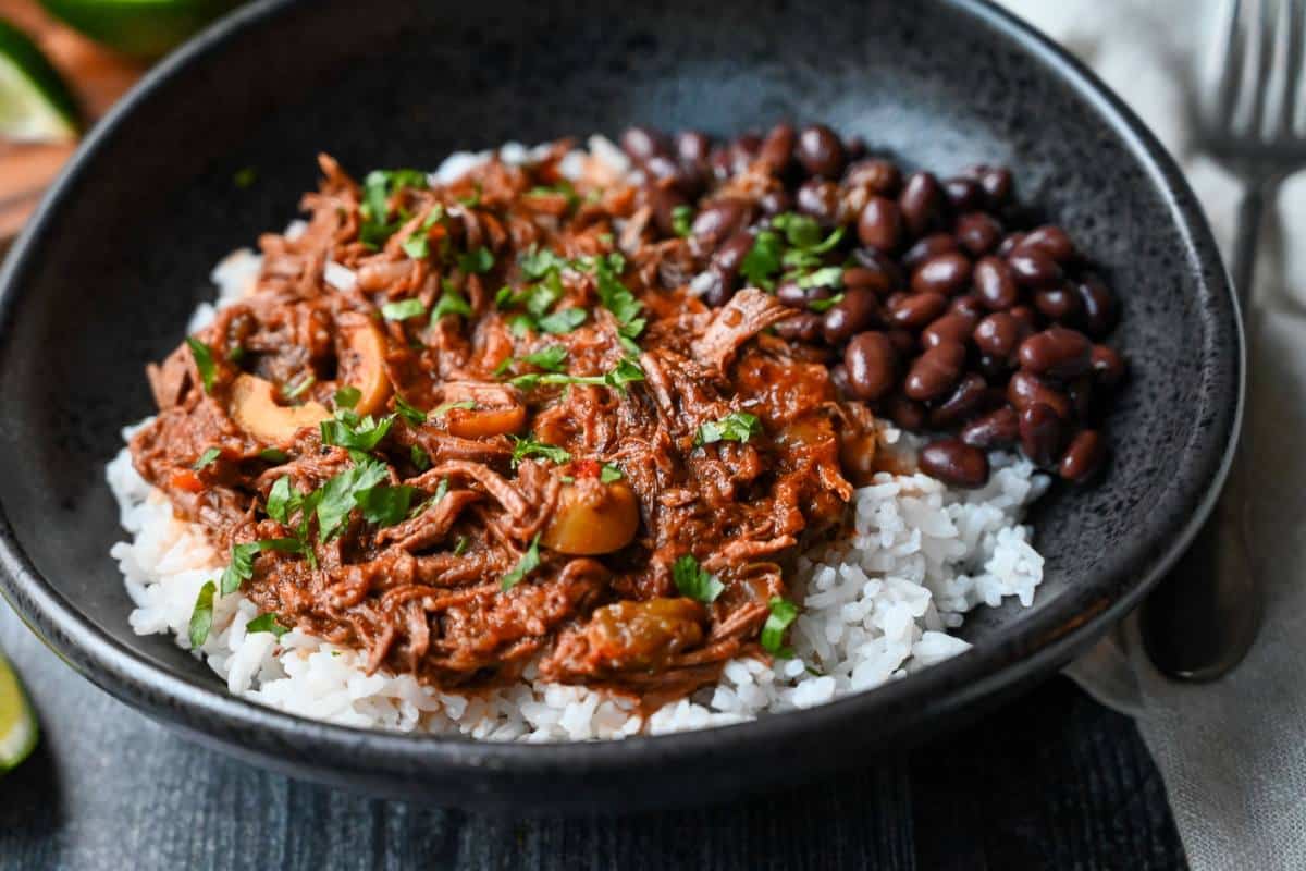 side view of a bowl of cuban beef with a napkin and fork